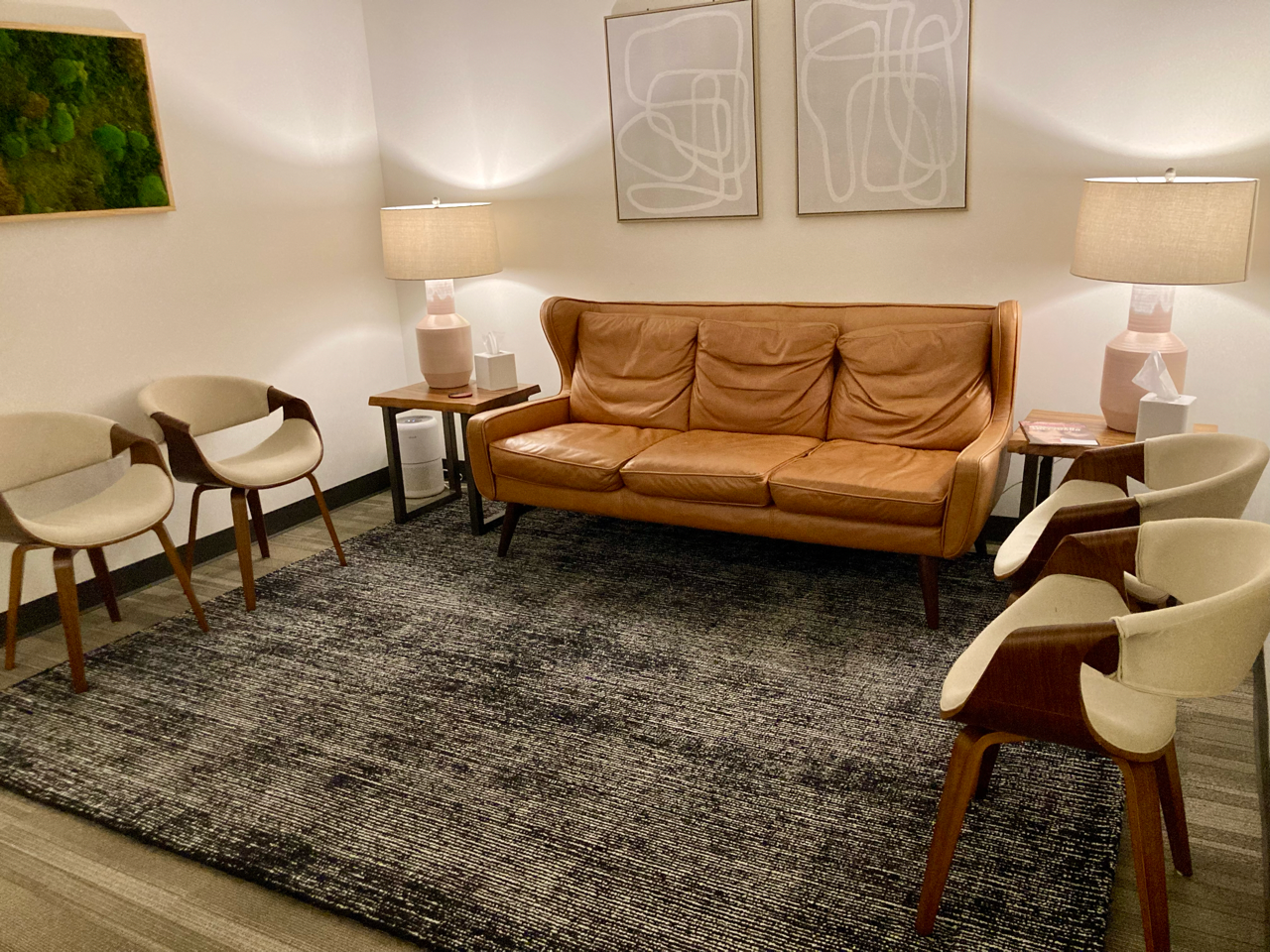 Waiting room with leather sofa, two chairs, rug, lamps, and wall art.