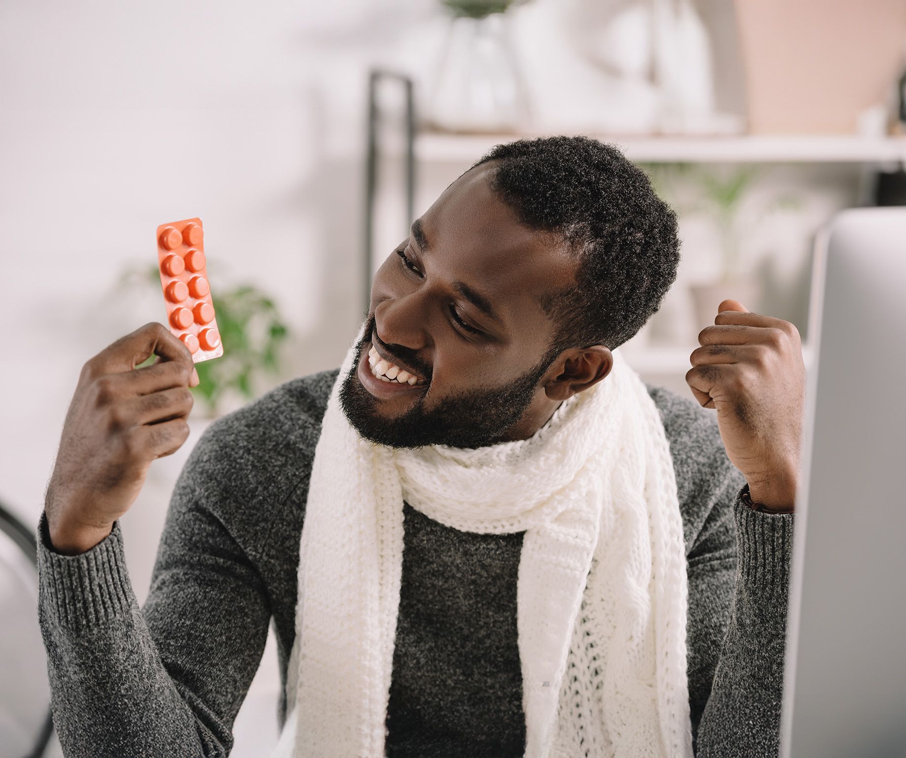 Man with a white scarf celebrates, holding an orange blister pack of pills.