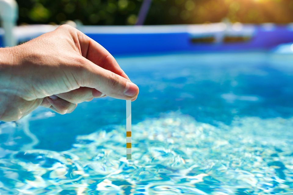 Mano che tiene una striscia reattiva sopra una piscina blu, per controllare la qualità dell'acqua.