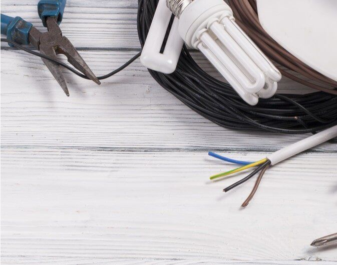 A pair of pliers a light bulb and a bunch of wires on a table - Electrician in Emerald | All Saints Electrical