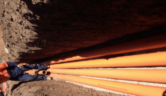 A man is standing next to a pile of pipes in the dirt- Electrician in Emerald | All Saints Electrical