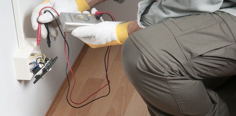 A man is kneeling down while holding a voltage meter - Electrician in Emerald | All Saints Electrical