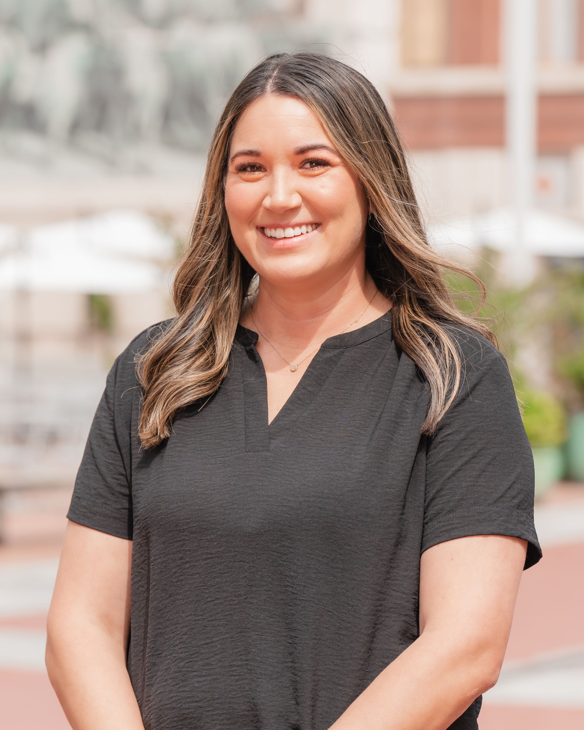 A woman in a black shirt is smiling and standing in front of a building.