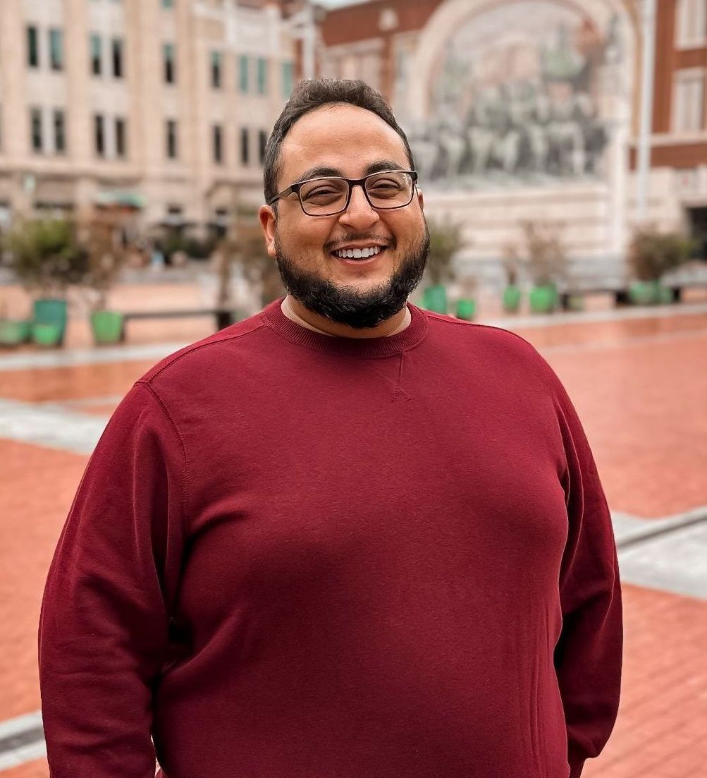 A man with a beard and glasses is wearing a red sweater and smiling.