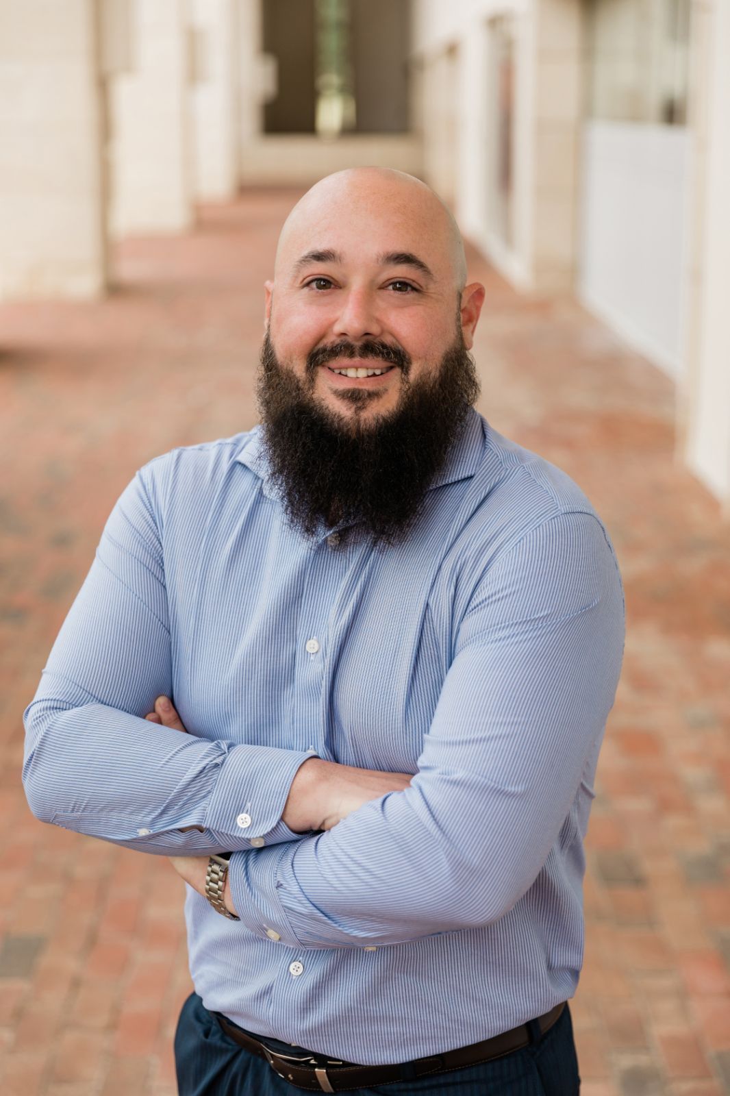 A bald man with a beard is standing with his arms crossed.
