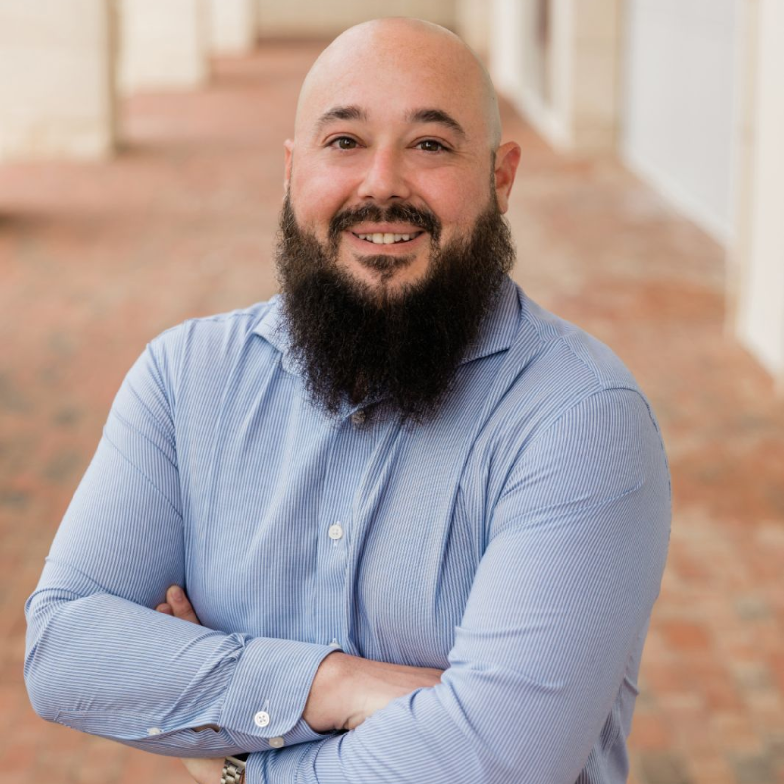 A bald man with a beard is standing with his arms crossed.