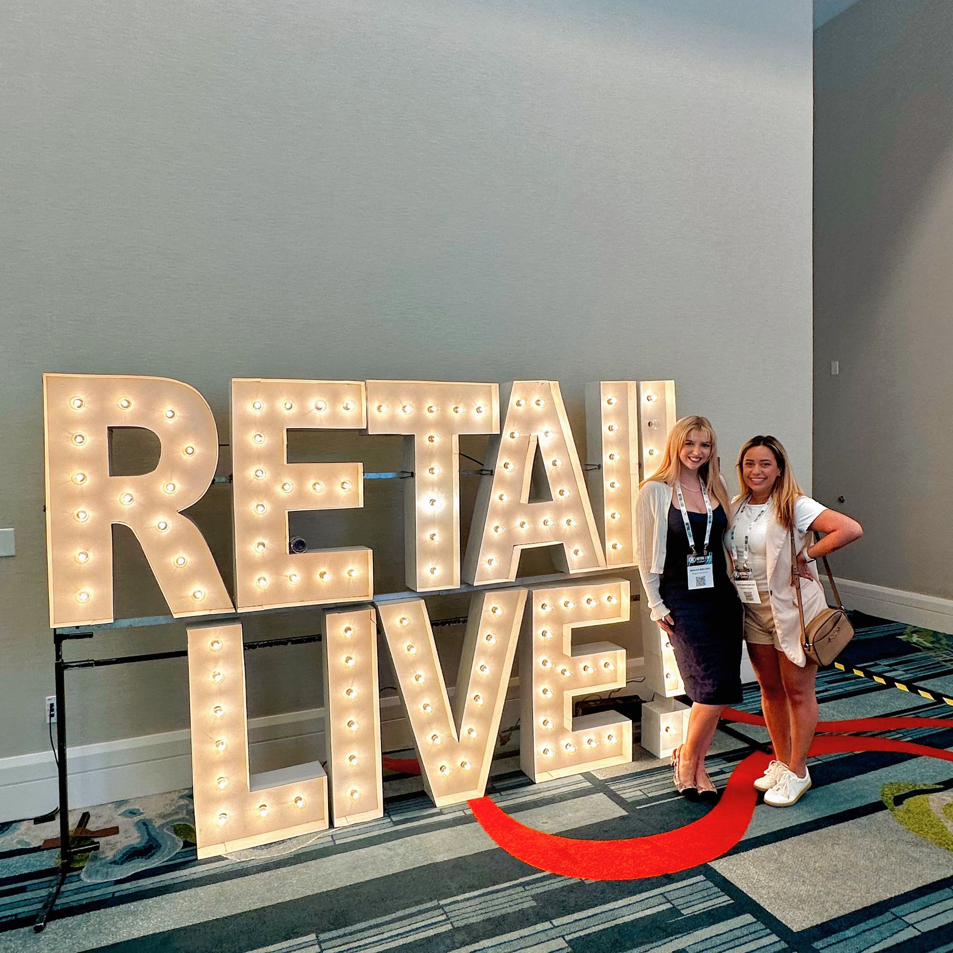 Two women standing in front of a sign that says retail live