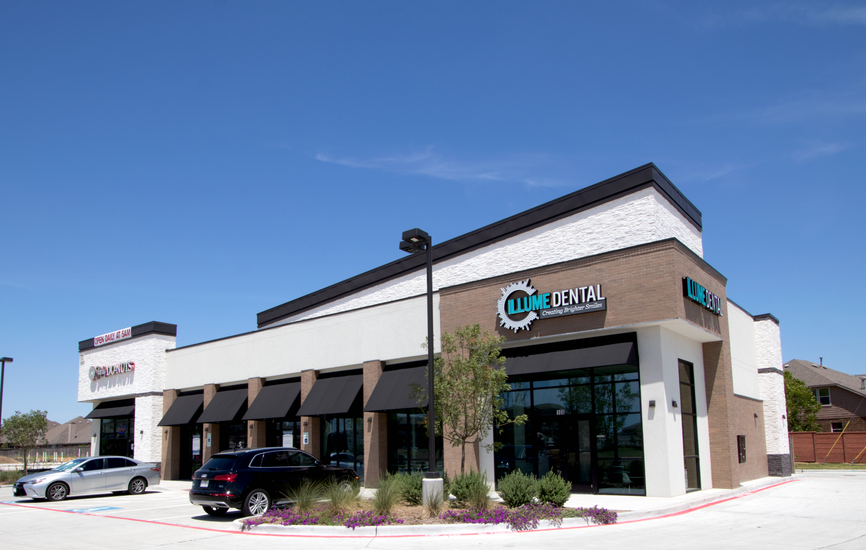 A white and brown building with cars parked in front of it.