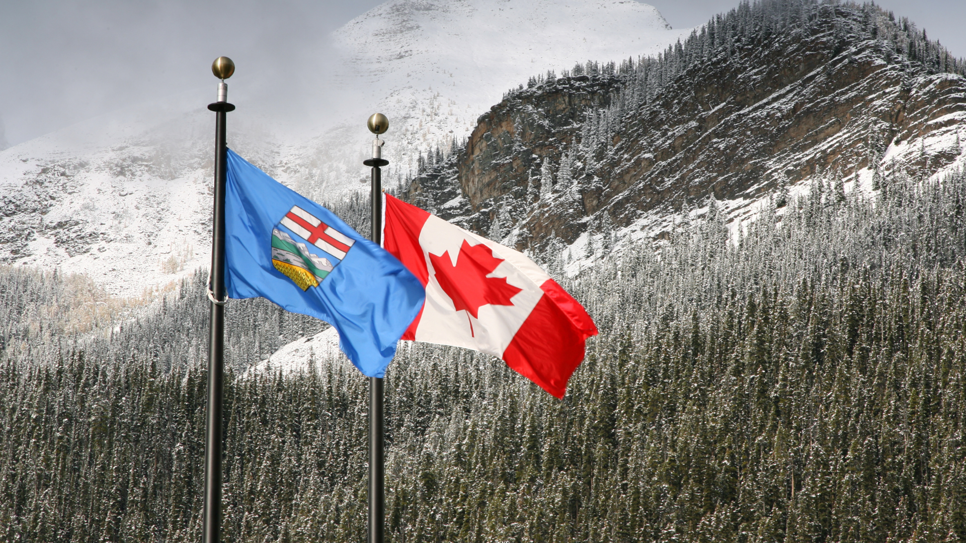 Alberta flag and Canadian flag waving against a snowy mountain backdrop.