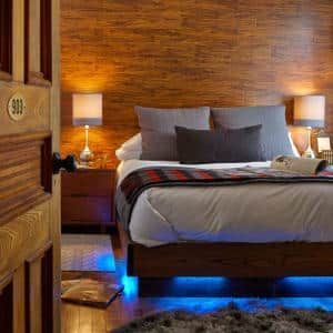 A bedroom with a bed , lamps , nightstands and a wooden wall.