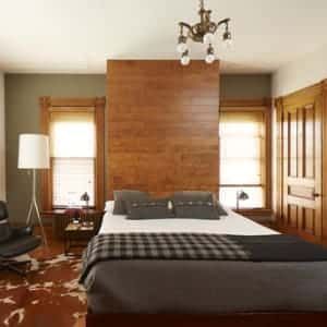 A bedroom with a bed , chair , lamp and a wooden wall.