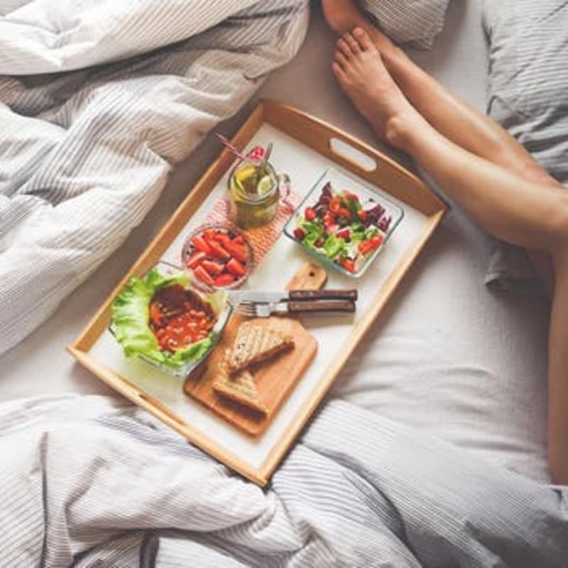 A woman is laying in bed with a tray of food on it