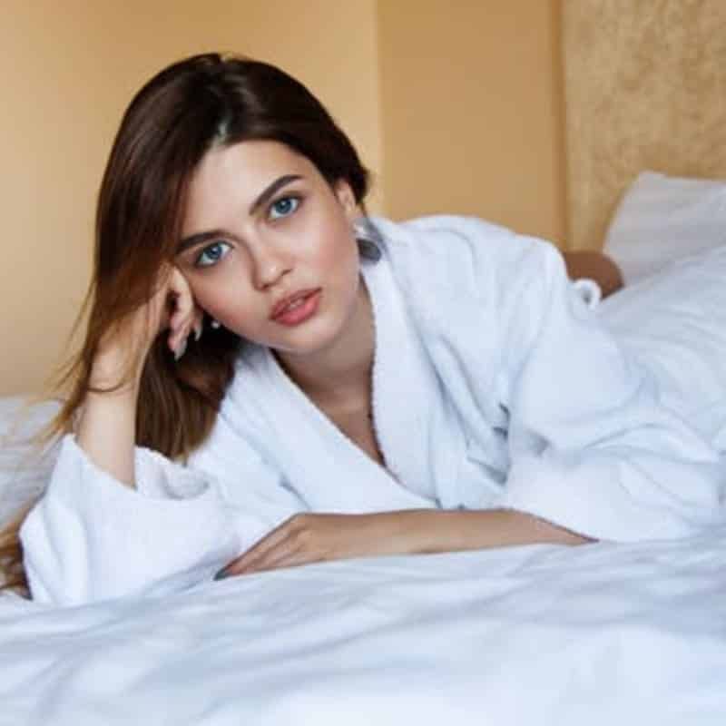 A woman in a white robe is laying on a bed.