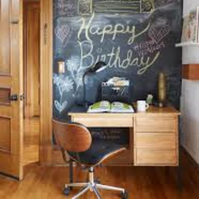 A room with a desk and chair and a chalkboard wall that says `` happy birthday ''.