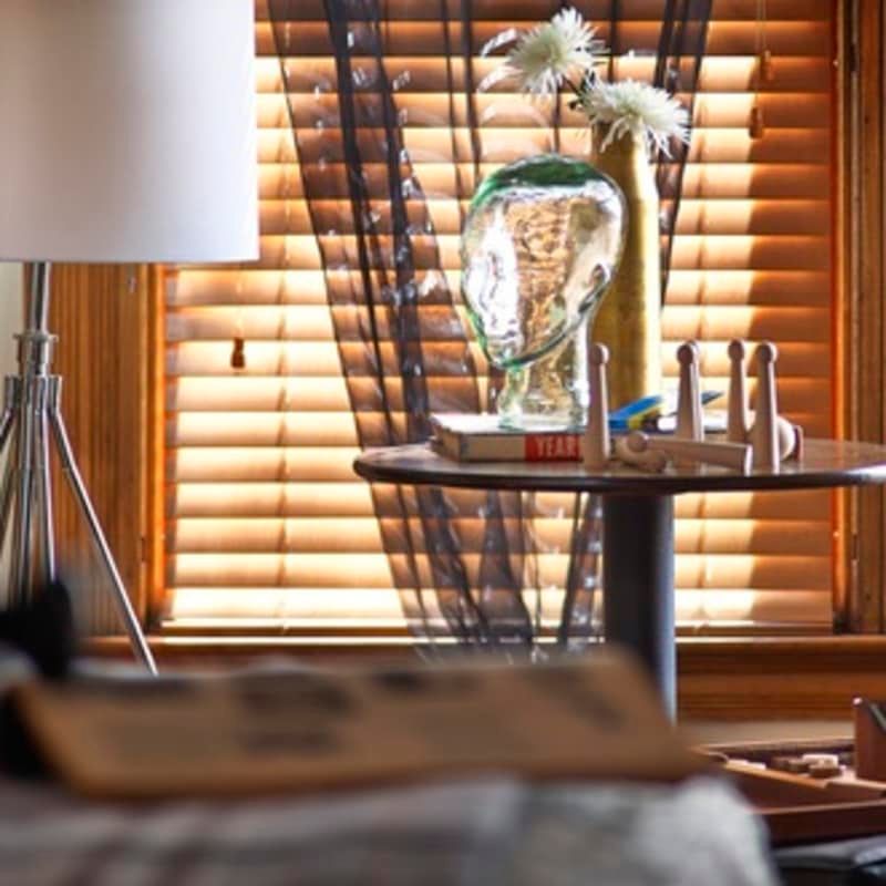 A vase of flowers sits on a table in front of a window with blinds
