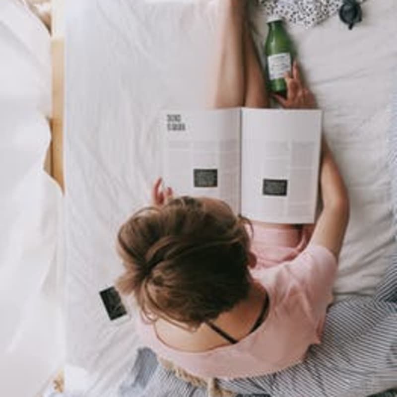 A woman is laying on a bed reading a book and holding a bottle of water.