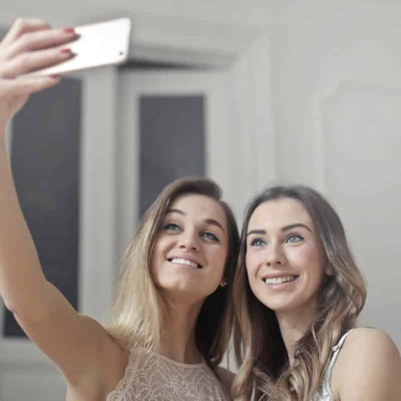 Two women are taking a selfie together with a cell phone.
