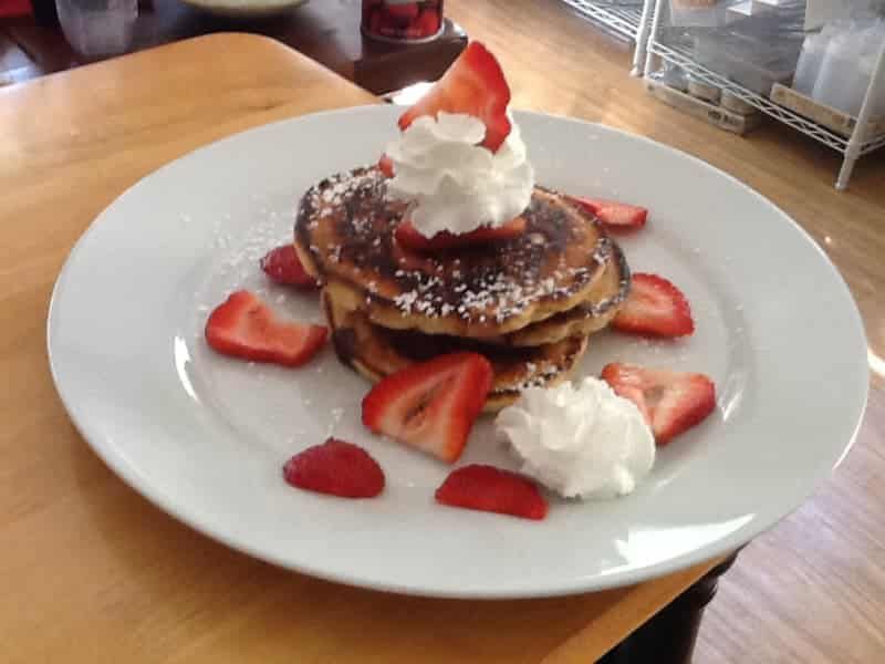 A stack of pancakes with whipped cream and strawberries on a white plate