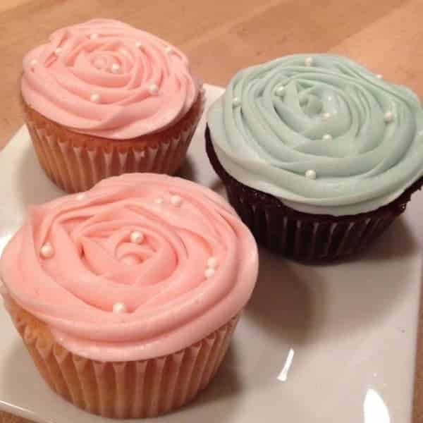 Three cupcakes with pink frosting and pearls on a white plate