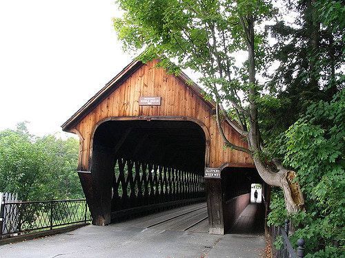 A wooden covered bridge is surrounded by trees on a cloudy day