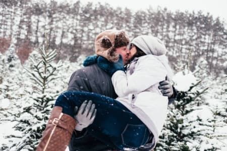 A man is carrying a woman in his arms and they are kissing in the snow.