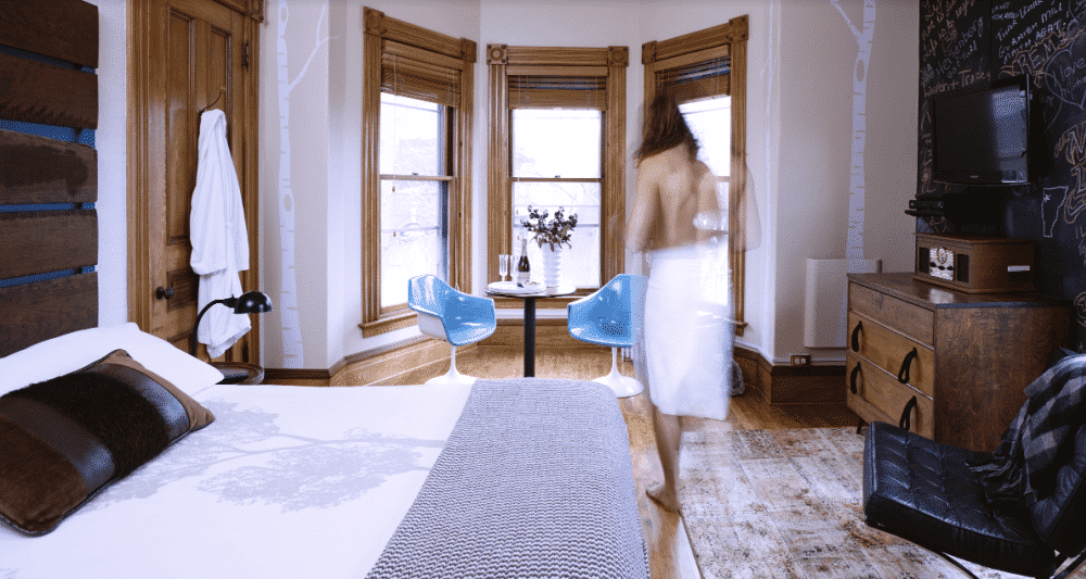 A woman in a towel is standing in a bedroom next to a bed.
