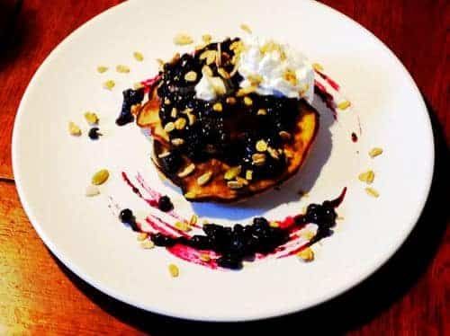 A white plate topped with a pancake with blueberry sauce and whipped cream.