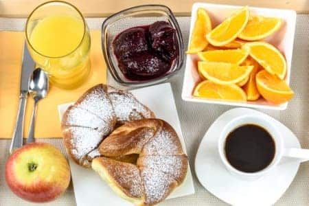 A table topped with a variety of food , including croissants , fruit , juice and coffee.