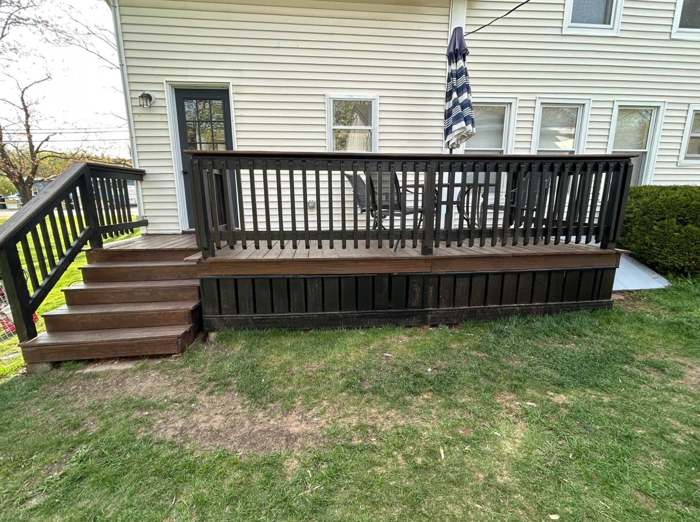 A composite deck with a dining area, steps, and a grill, attached to a house with an umbrella.