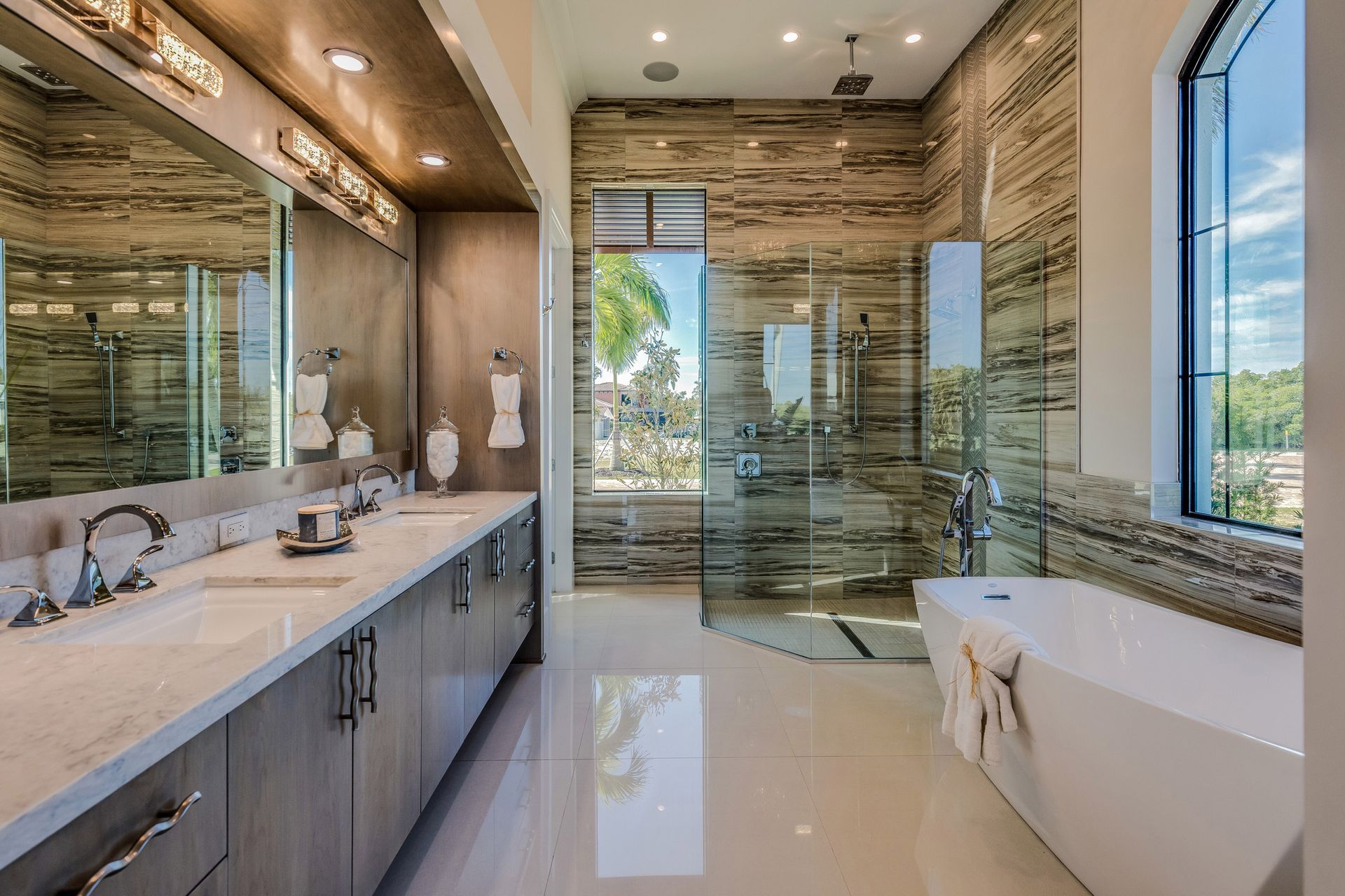 Luxurious modern bathroom with marble vanity, soaking tub, glass shower, and large windows.