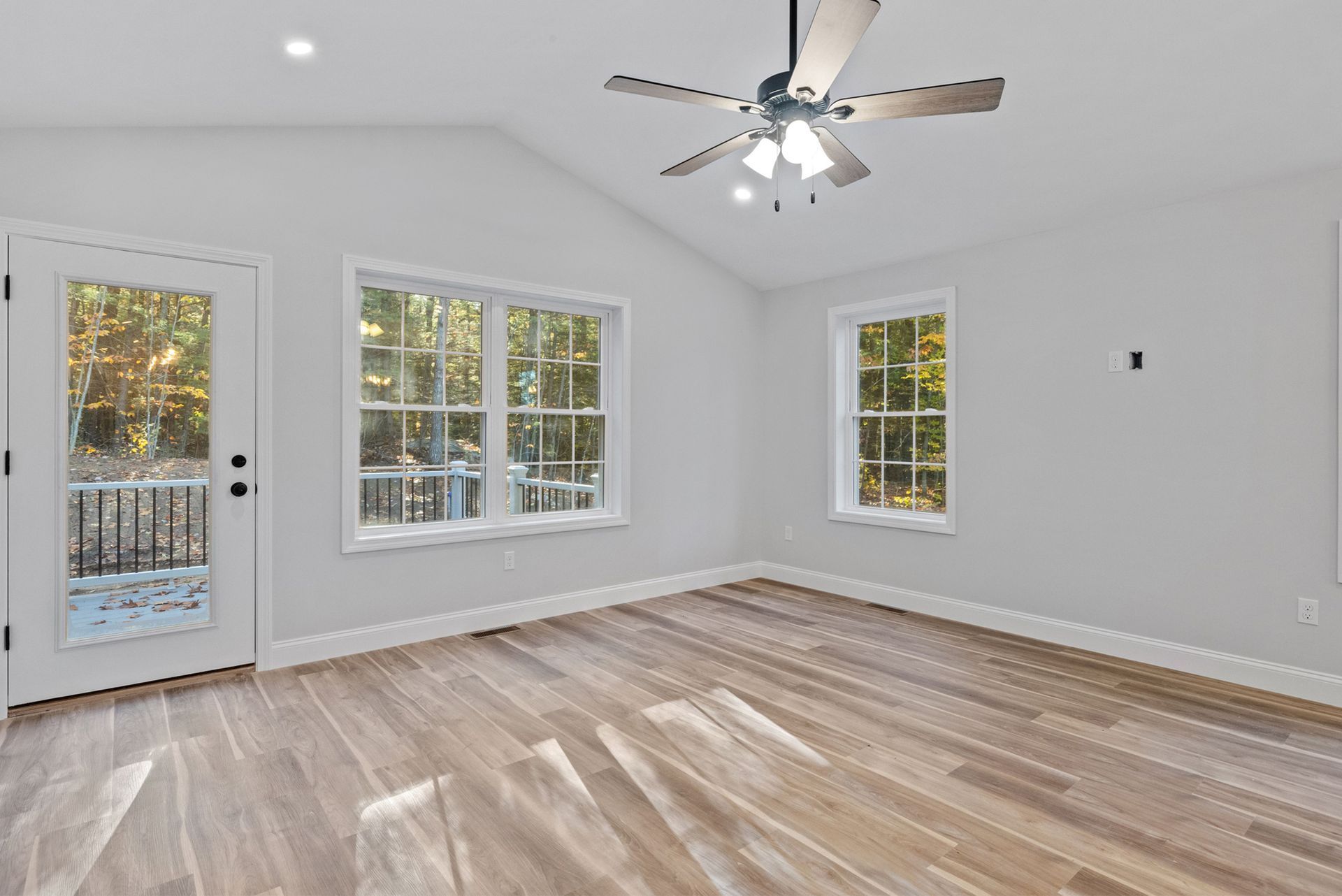 Empty room with wooden floor, windows, and a ceiling fan.