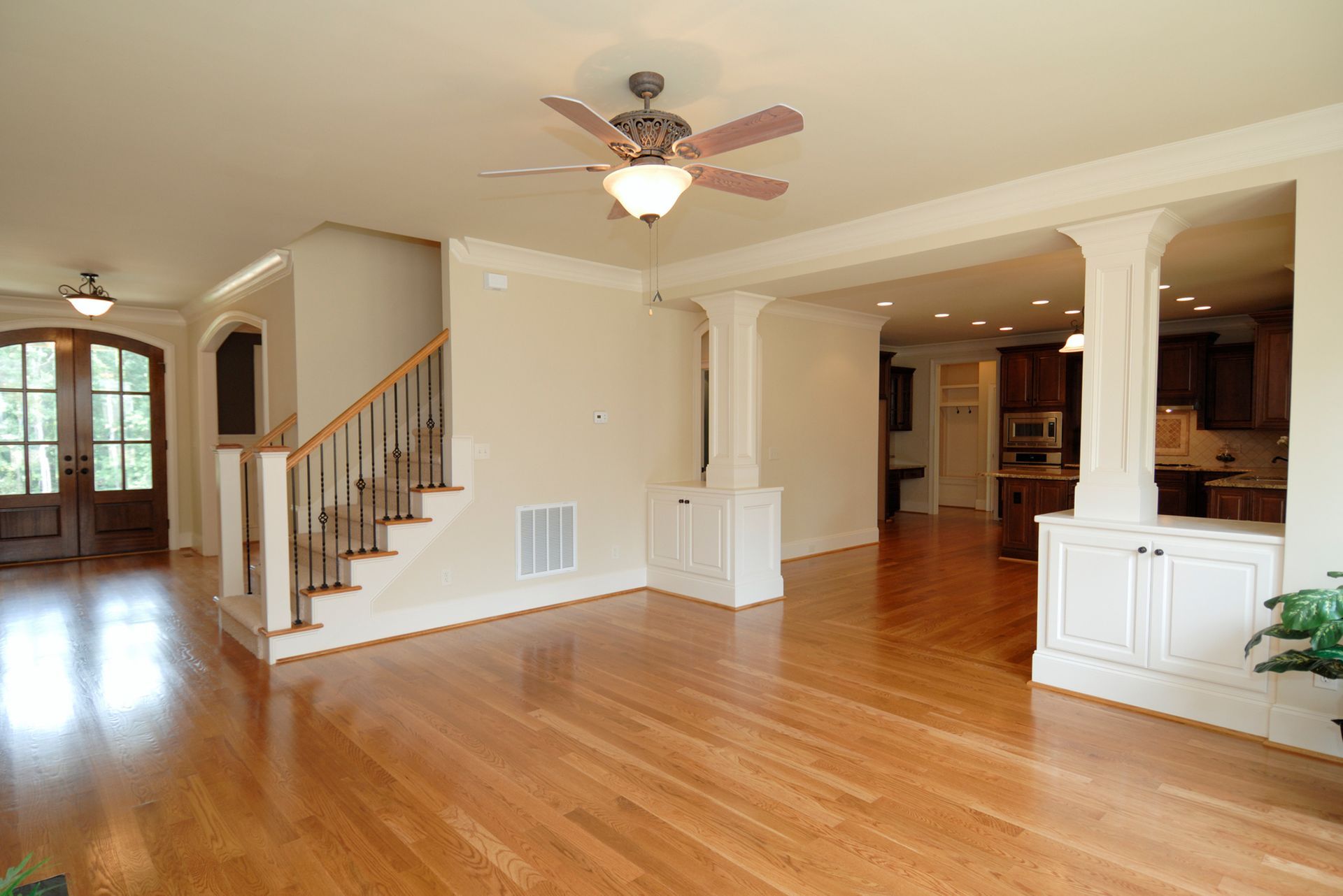 Spacious living room with hardwood floors, staircase, columns, and a view of the kitchen.