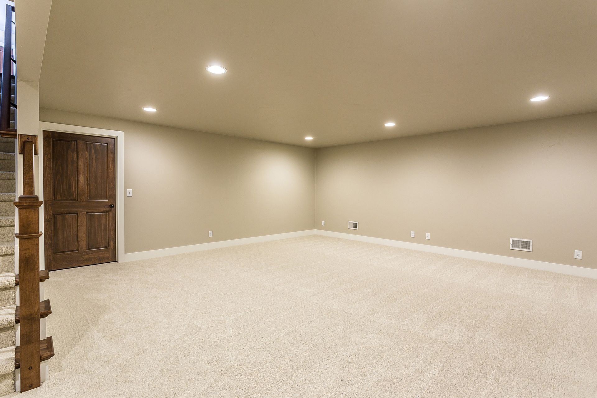 Empty beige room with carpet, a wooden door, and recessed ceiling lights.