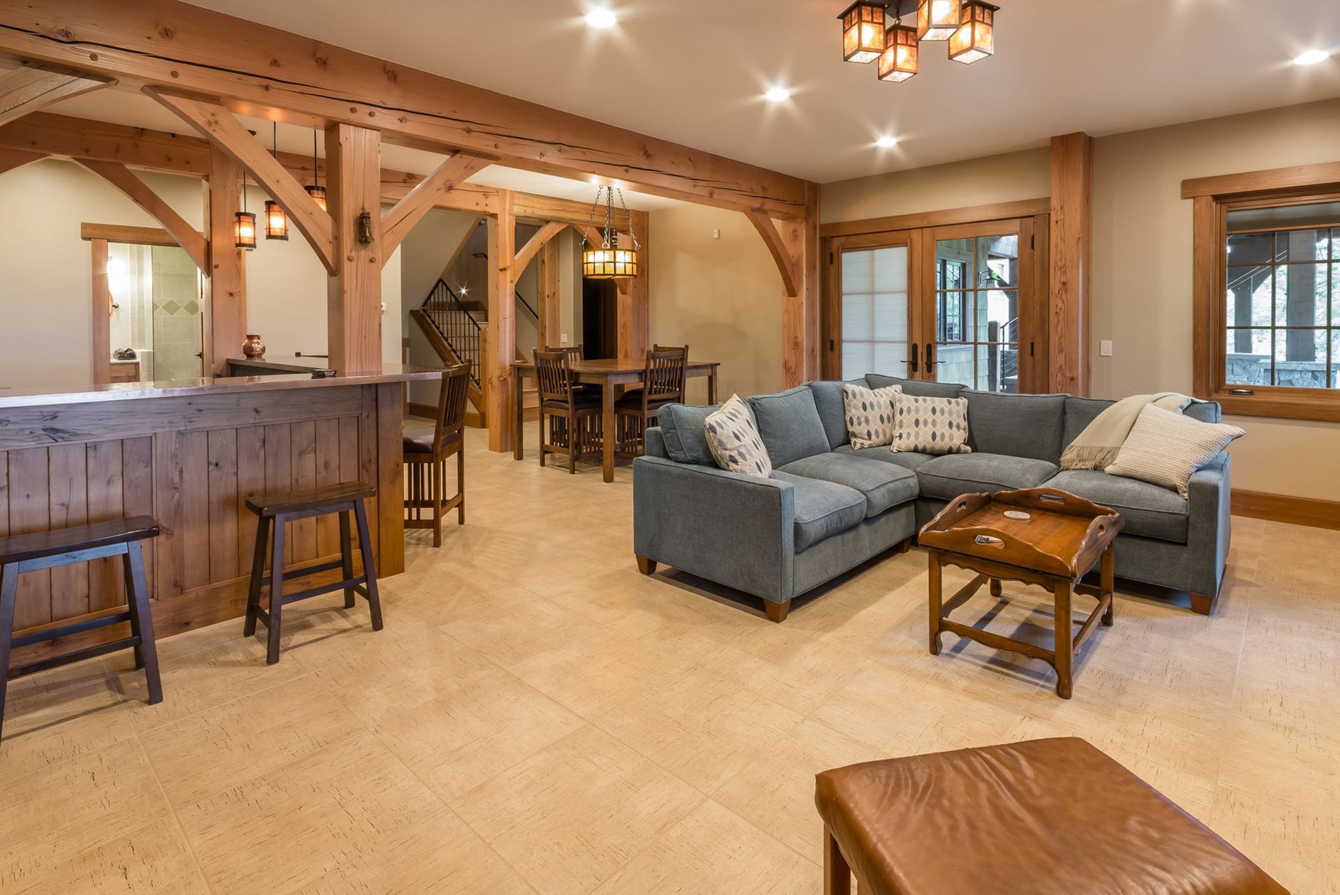 Spacious rustic living area with a blue sectional, bar, and dining table, wood beams, and neutral tones.