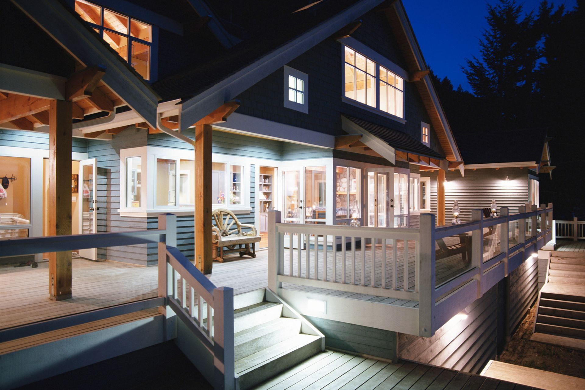 Night view of a house with a deck, lit windows, and stairs.