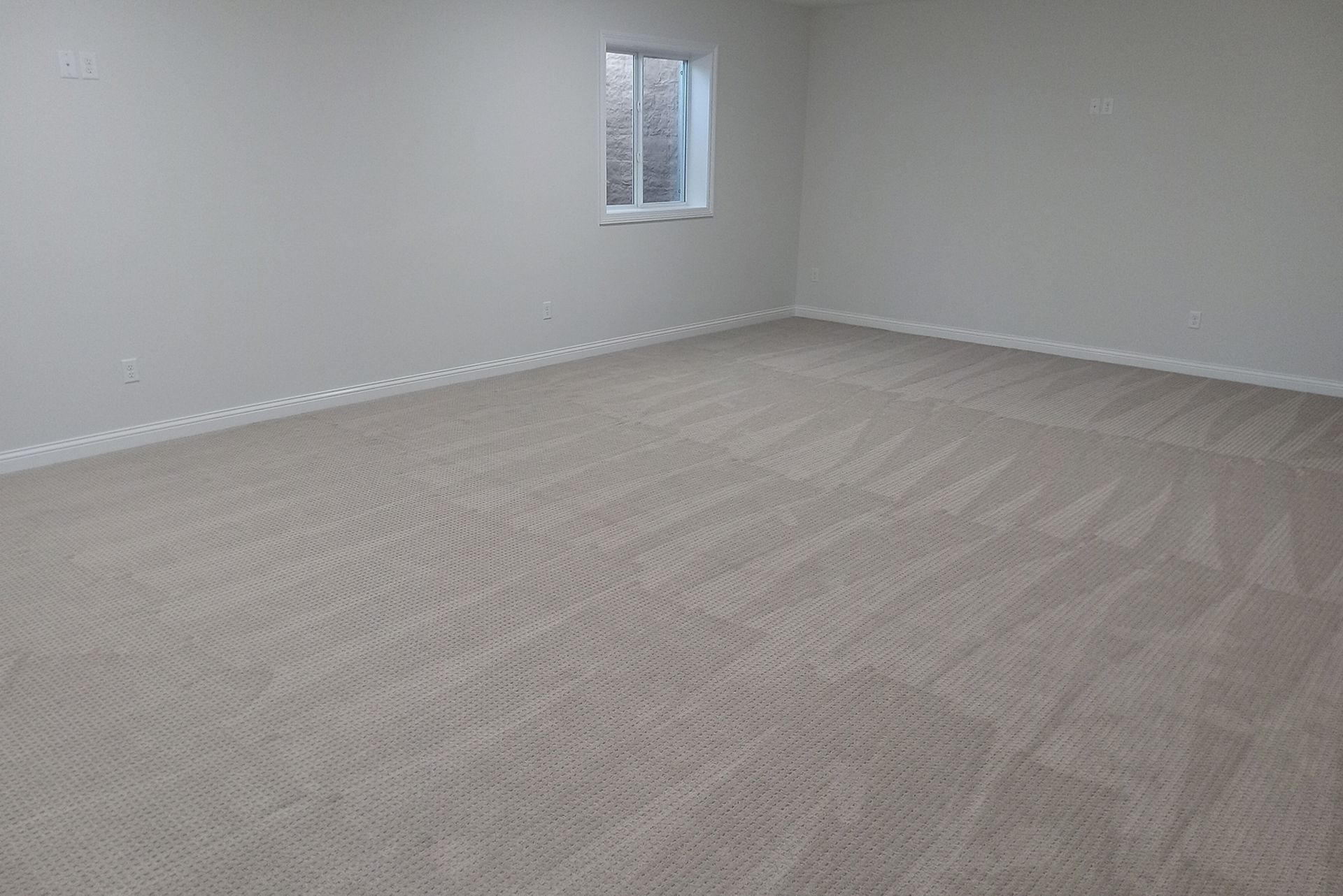 Empty room with beige carpet and off-white walls. Small window on the far wall.