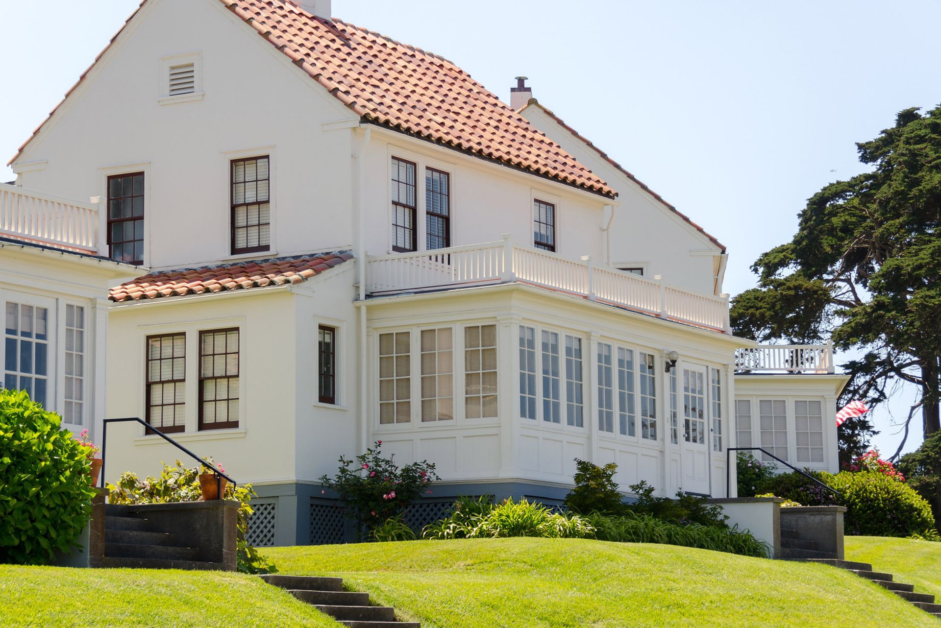 White house with orange tile roof, surrounded by green grass and trees on a sunny day.
