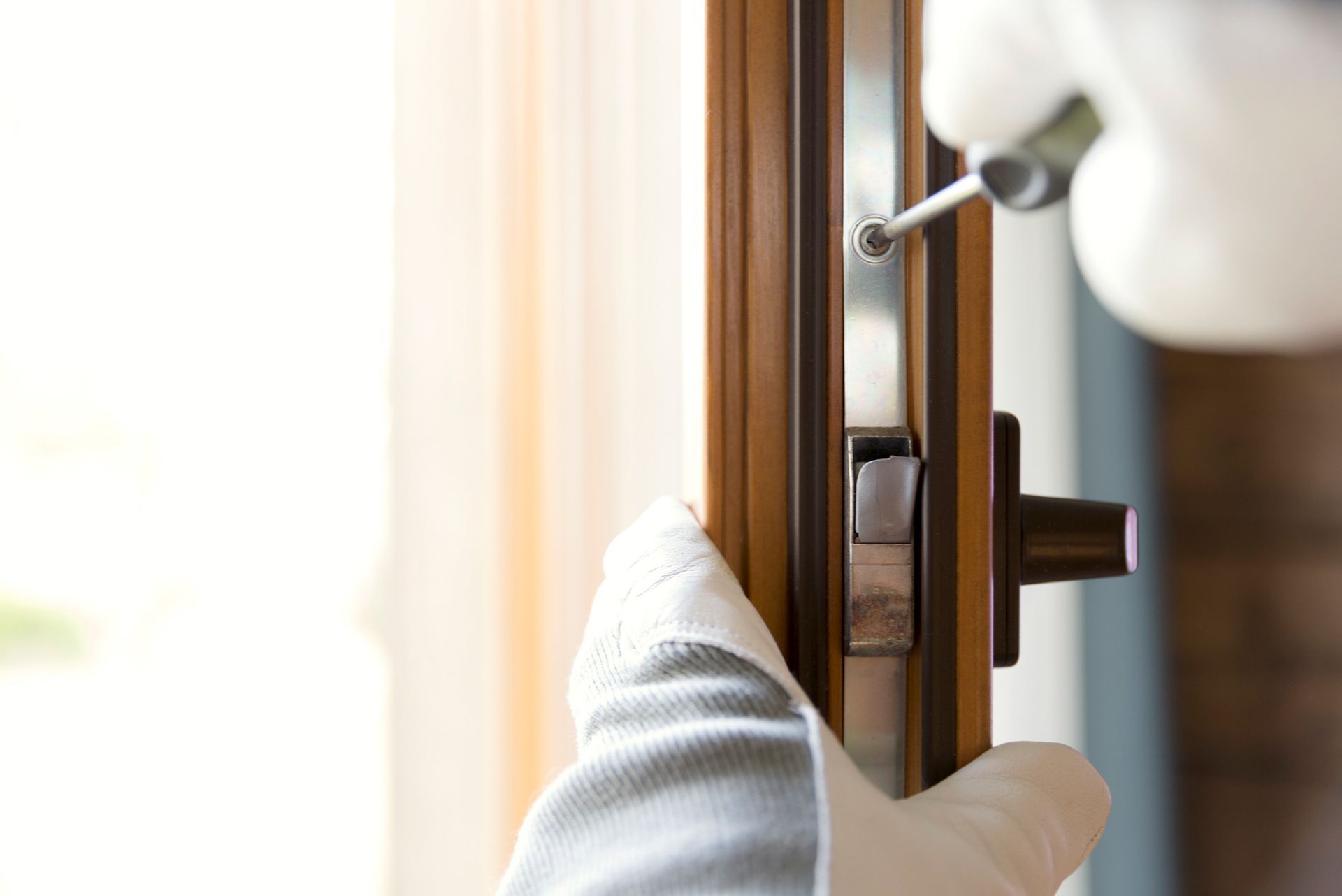 Person in gloves using a screwdriver to install a window lock.