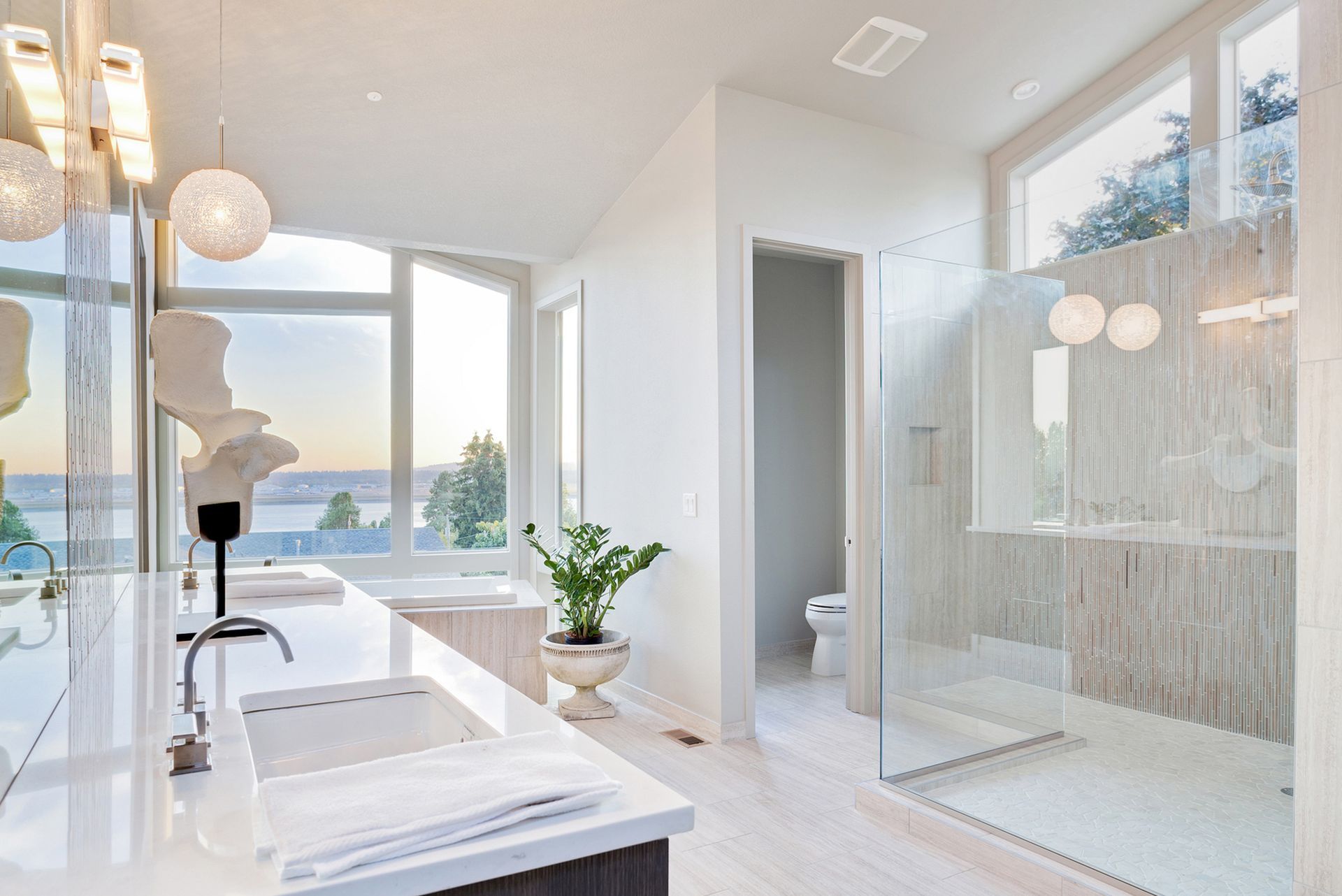 Bright white bathroom with large windows, a glass shower, and a view of a lake.