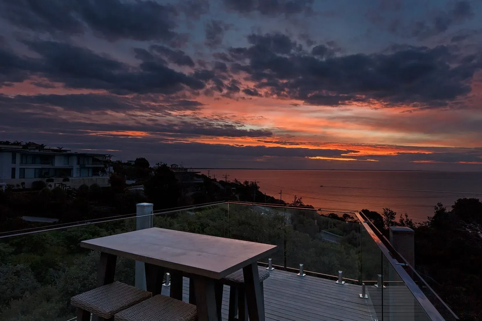 Rooftop deck with table overlooking ocean at sunset under dramatic clouds.