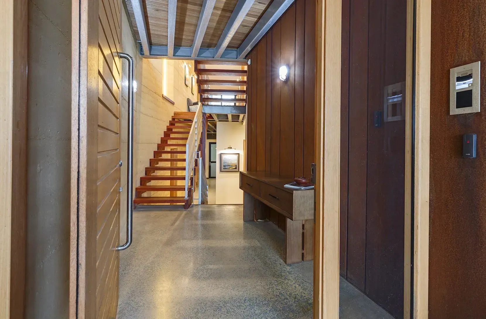 Entry hallway with timber stairs, polished concrete floor, and wood paneling.