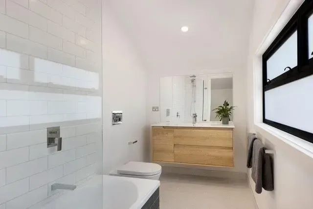 Bright bathroom with floating wood vanity, bathtub, and subway tile walls.