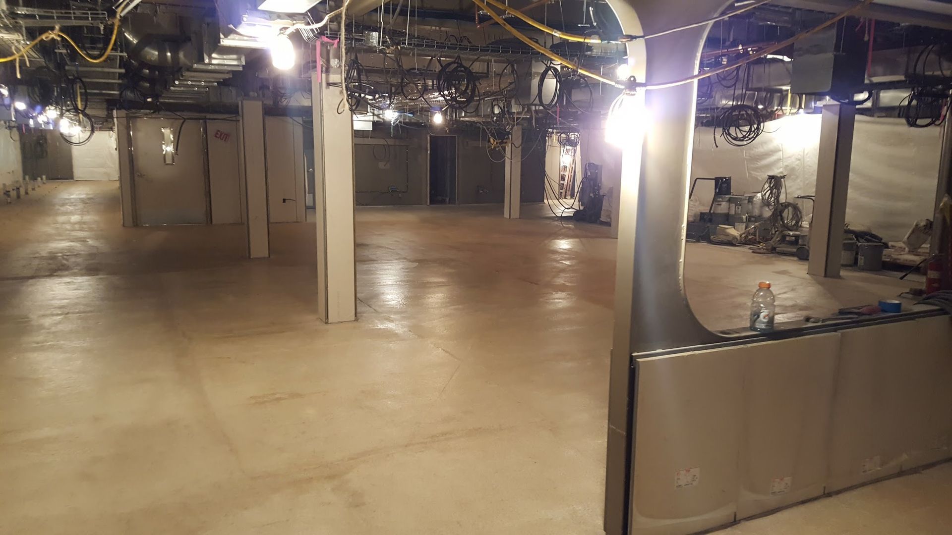 Large, empty, dimly lit room with concrete floor, pillars, and lights.