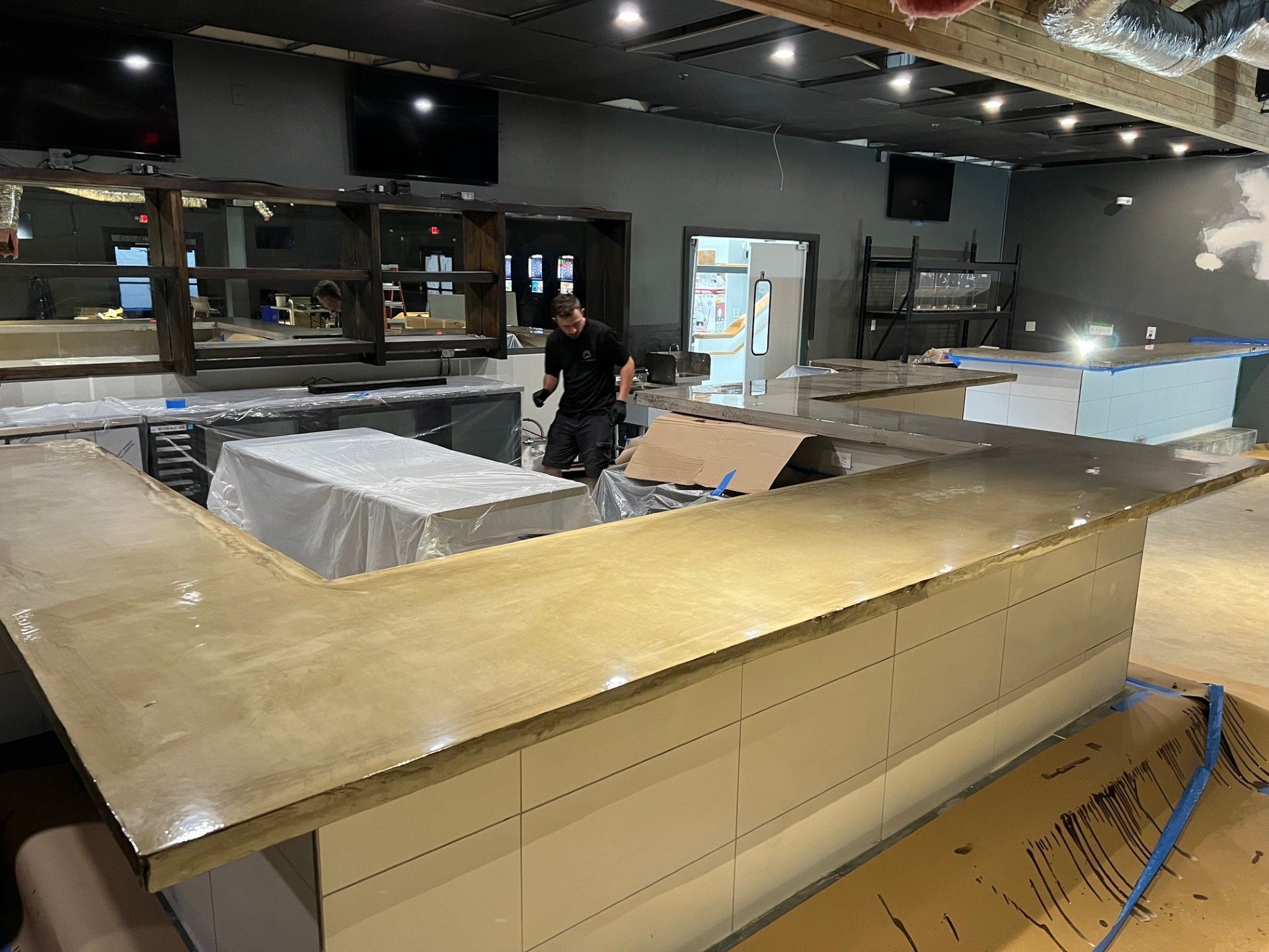 A person works at a U-shaped bar counter in a newly renovated bar with neutral colors.