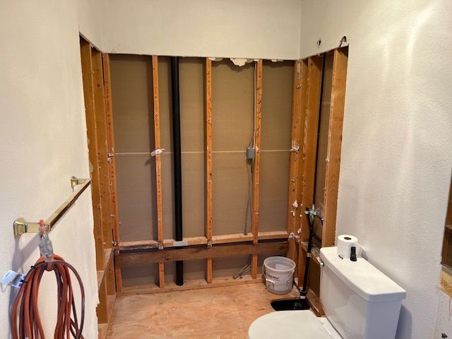 Bathroom renovation: exposed framing, plumbing, and toilet. Walls are open. Construction in progress.