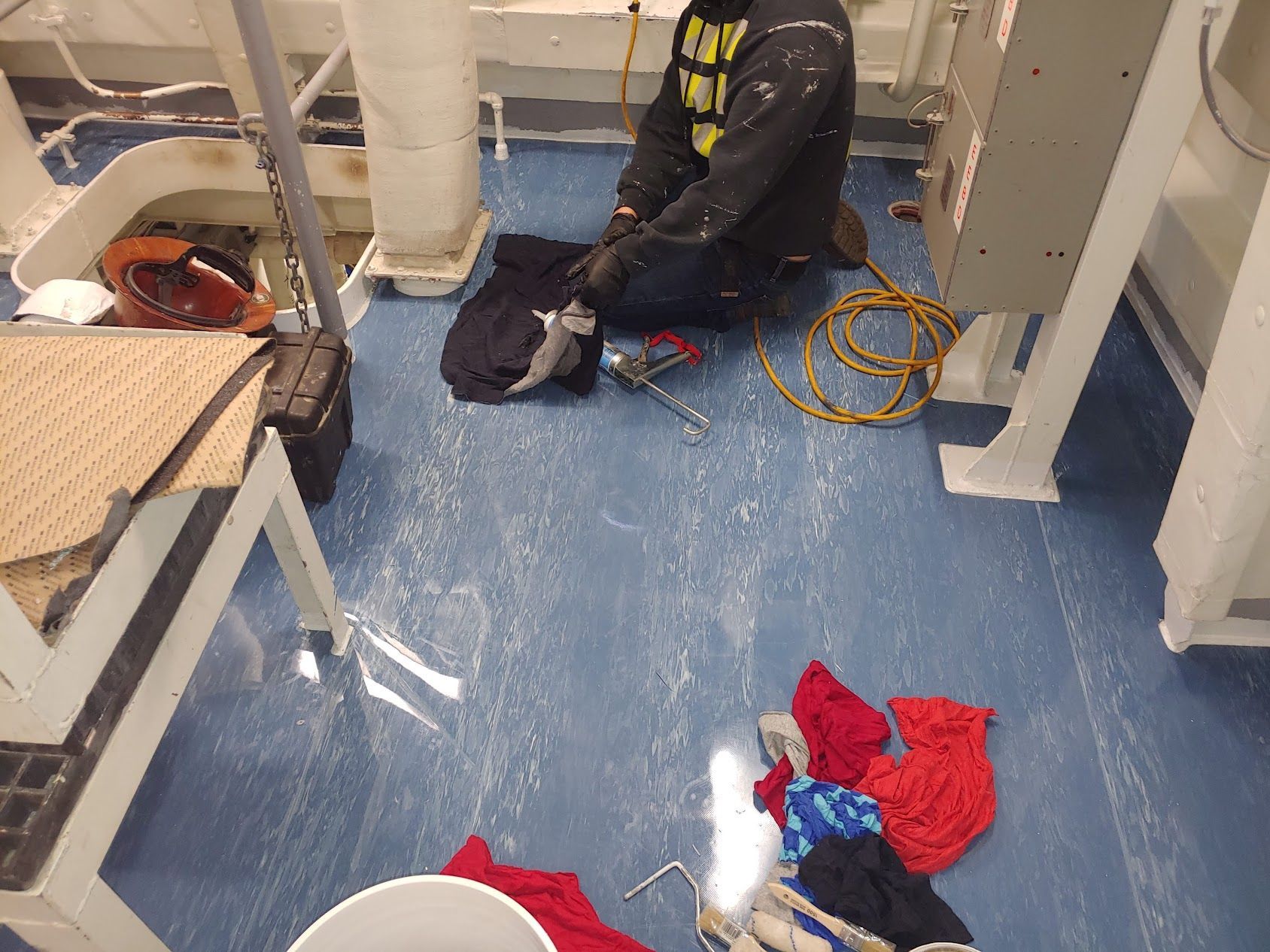 Person on blue floor with rags, tools. Setting appears industrial.