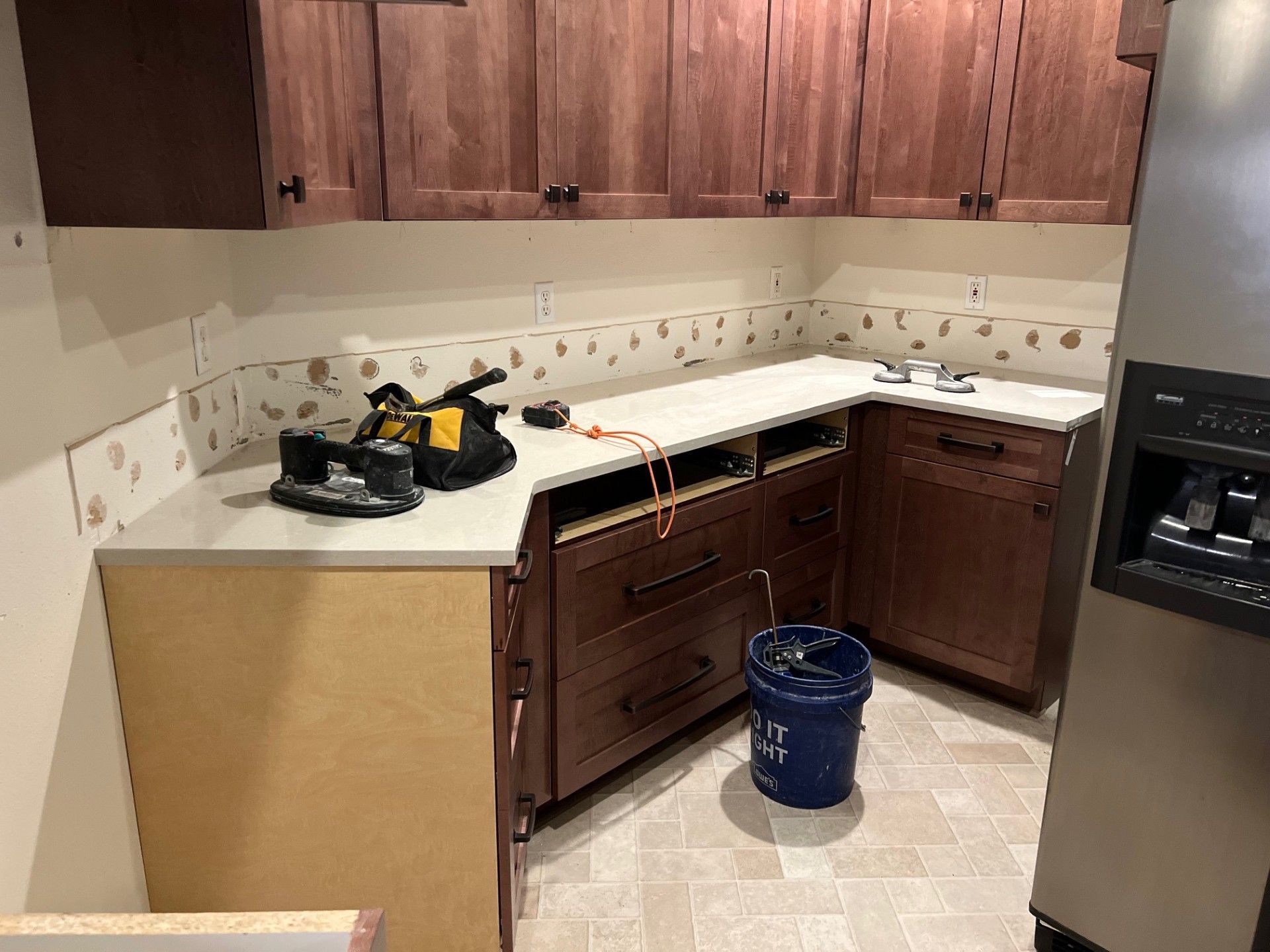 Kitchen renovation in progress: cabinets, countertop, tools, and a bucket on a light-colored floor.