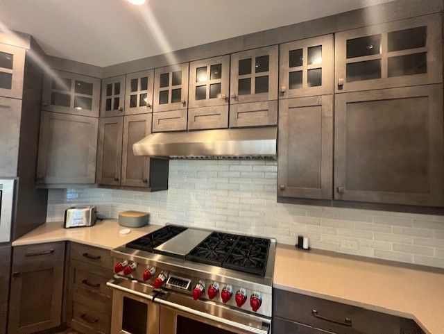 Kitchen with dark wood cabinets, stainless steel hood, stove, and off-white tile backsplash.