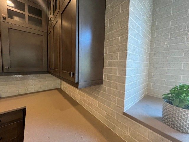 Dark cabinets above a tan countertop with matching brick-style backsplash. A potted plant sits in a niche.