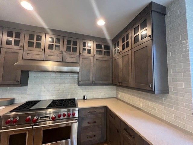 Gray kitchen with cabinetry, a stainless steel stove, and tiled backsplash.
